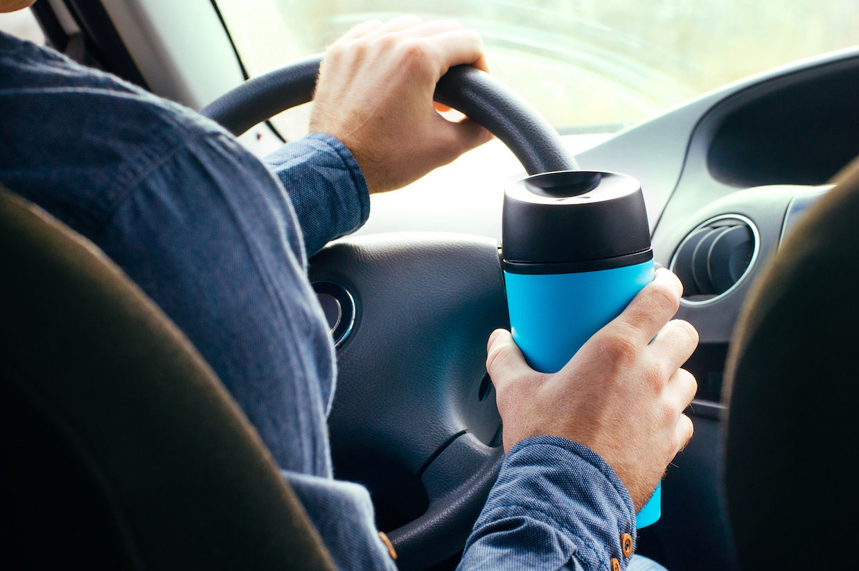 Man holding travel mug while driving